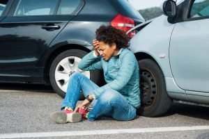A woman sitting on a road holding her head after a rear-end accident