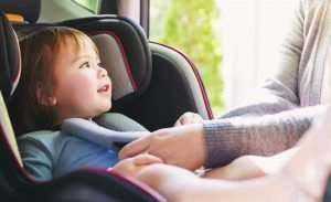 toddler girl getting buckled into her car seat